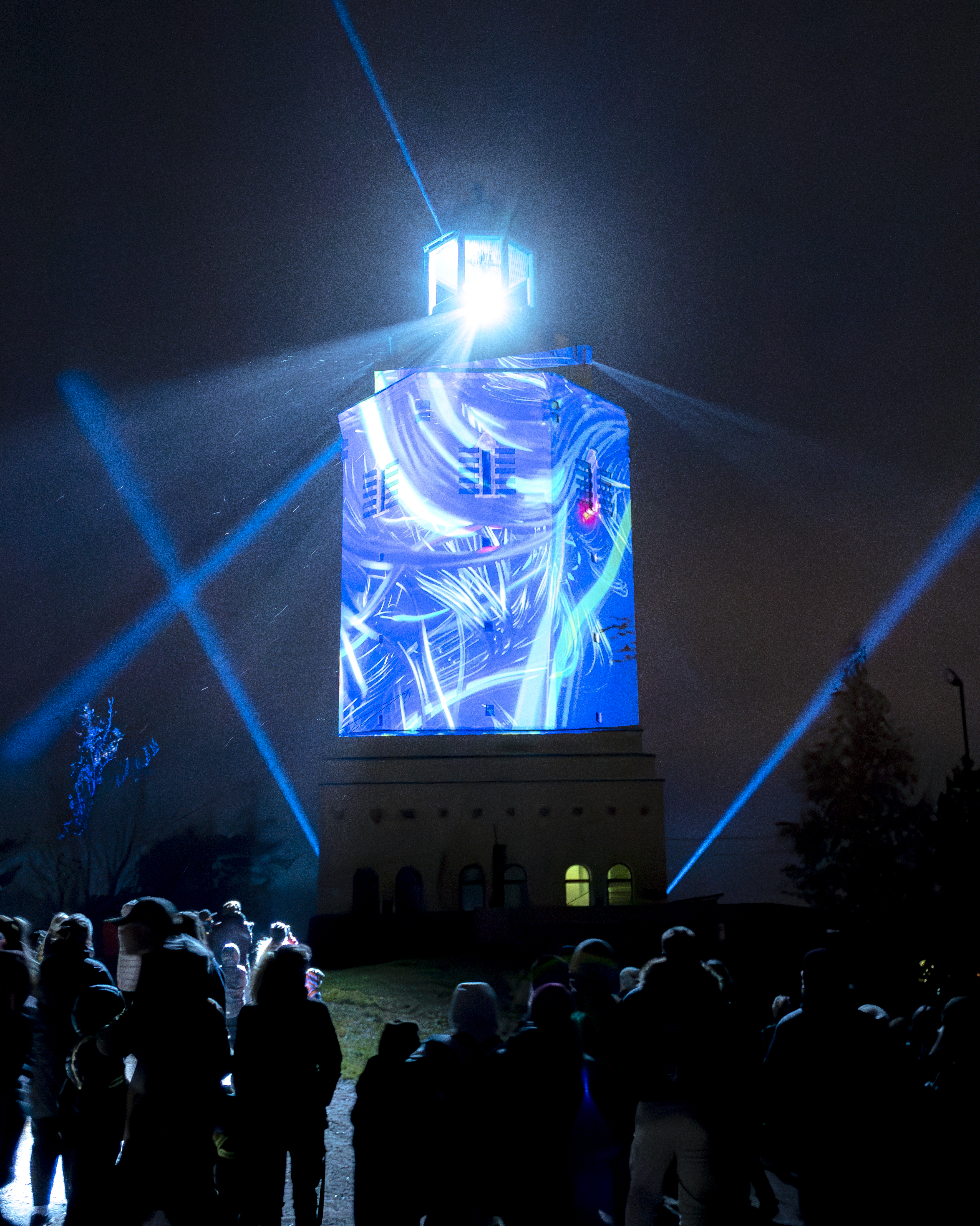 Kuvassa Haukkavuoren näkötorni valaistuna. Tornin edessä on joukko ihmisiä katselemassa tornia.